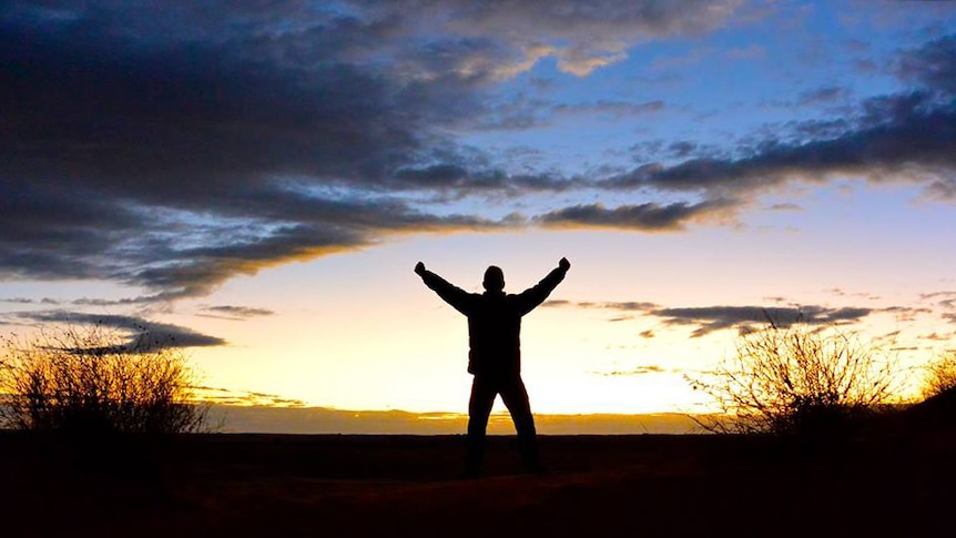 A man throws his arms in the air in the desert.