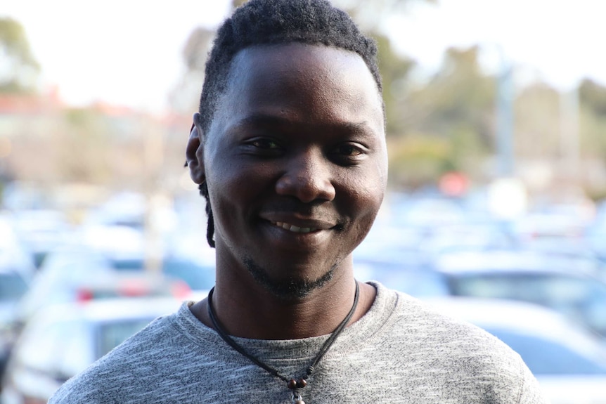 Alfred Noti, wears a leather necklace and tshirt, smiles at the camera.