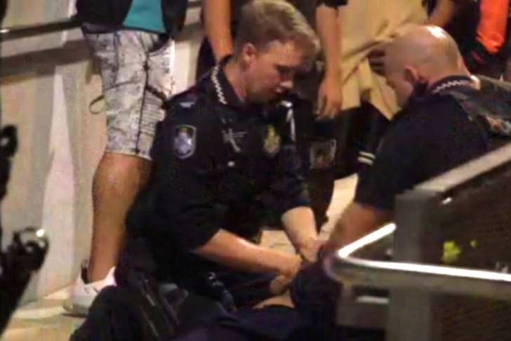 Police handcuff a teenager while he's on the ground.