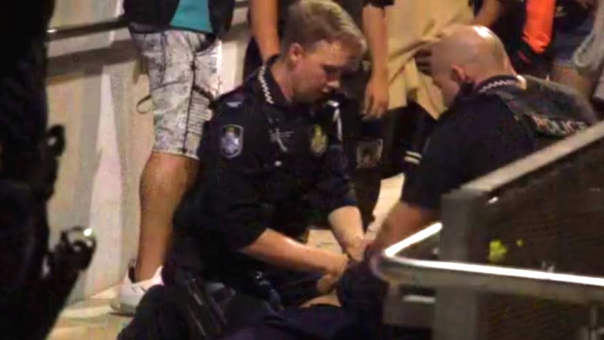 Police handcuff a teenager while he's on the ground.