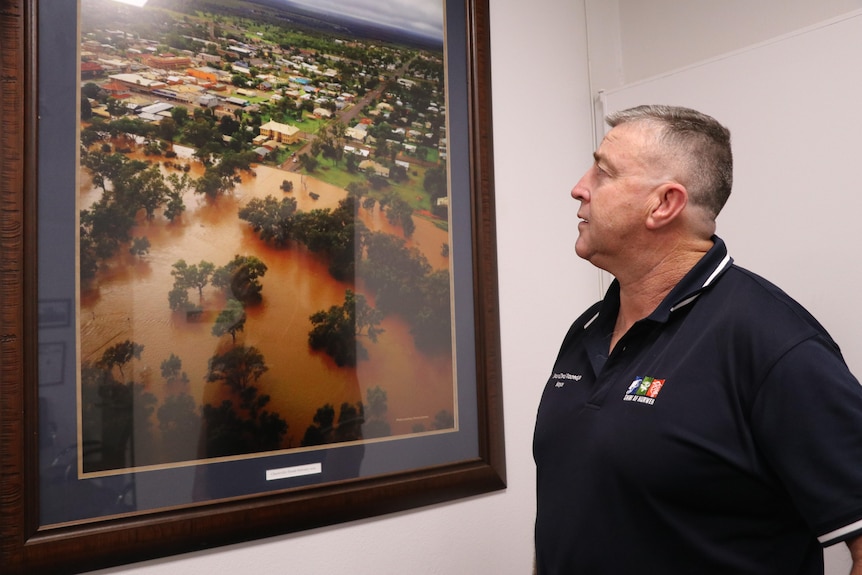 A man in a black shirt stands in front of a photo of a flooding event