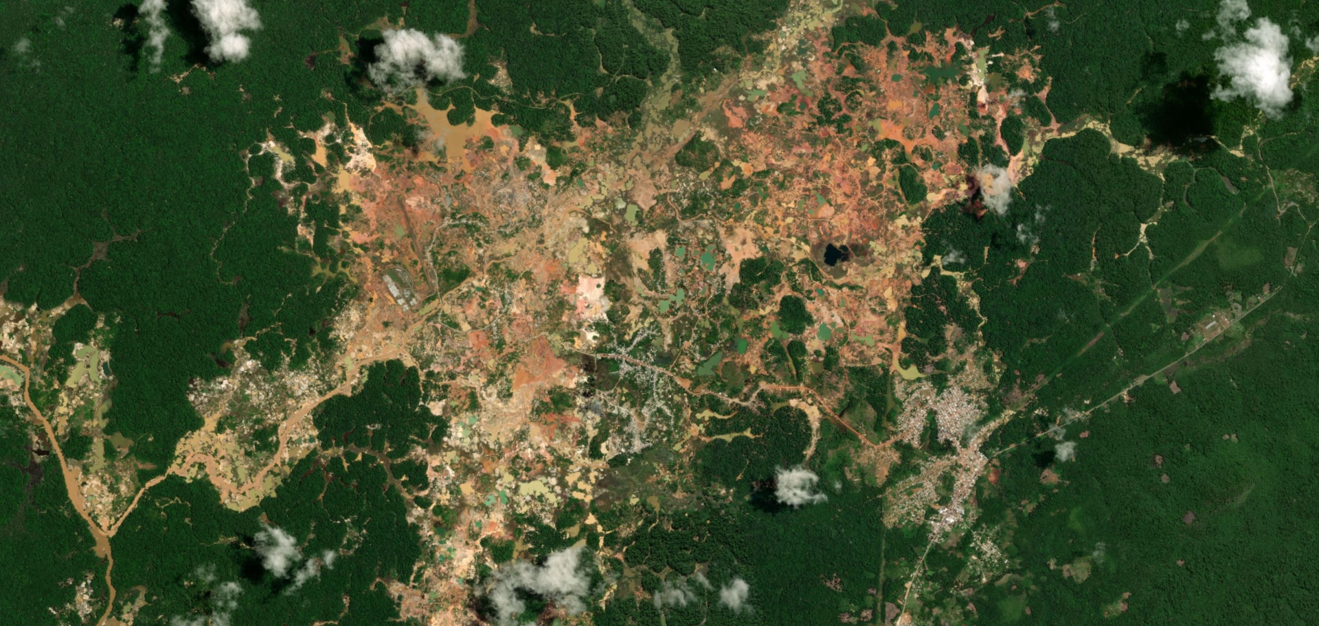 A sprawling orange-brown patch of mining land seen amid solid green Amazon forestry, seen from above.