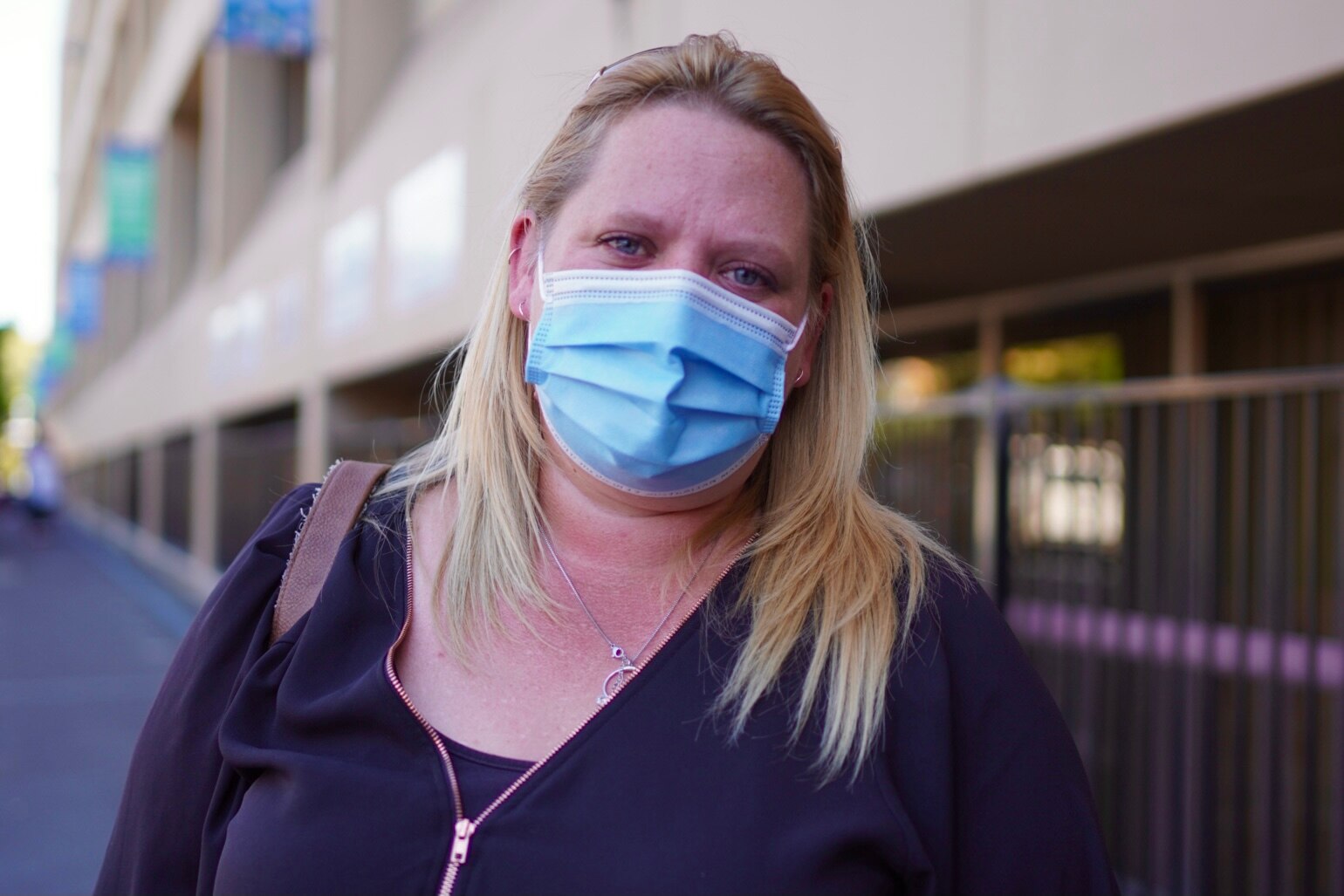 A blonde woman with long hair looks at the camera, she's wearing a face mask.