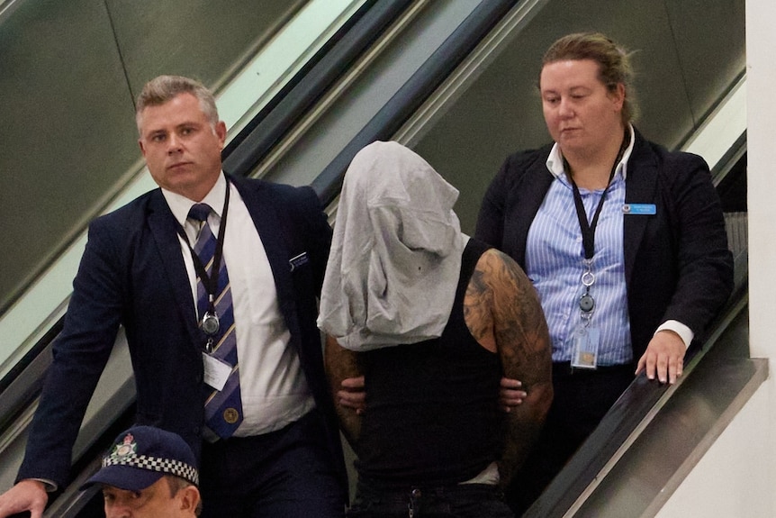 a man arrested by police and wearing a head covering