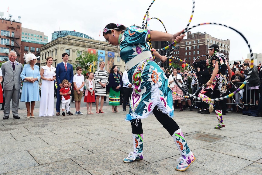 Indigenous dancers perform with hula hoops, watched by Prince Charles, Camilla, Justin Trudeau and his family.