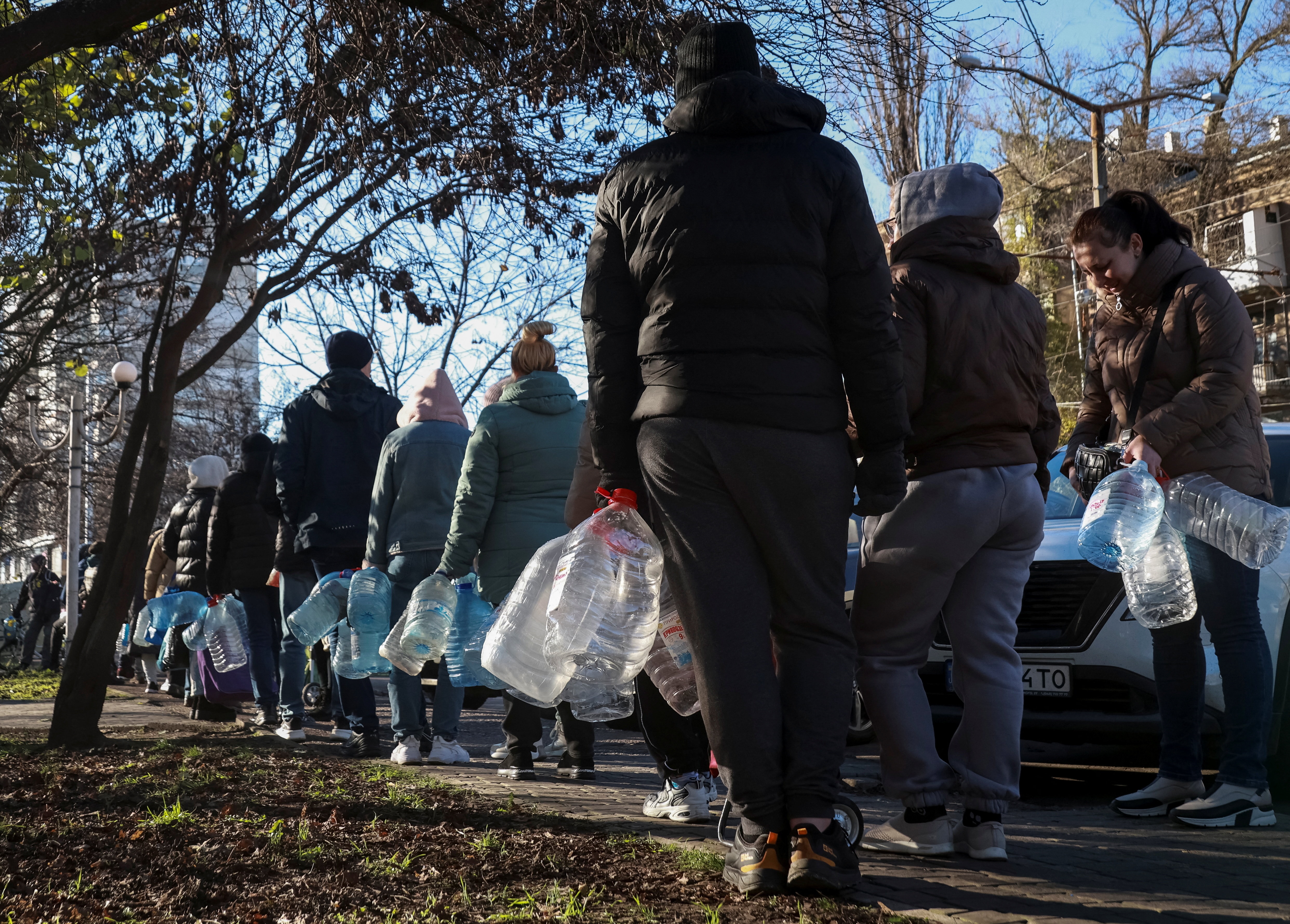 People stand in a queue holding large plastic bottles.