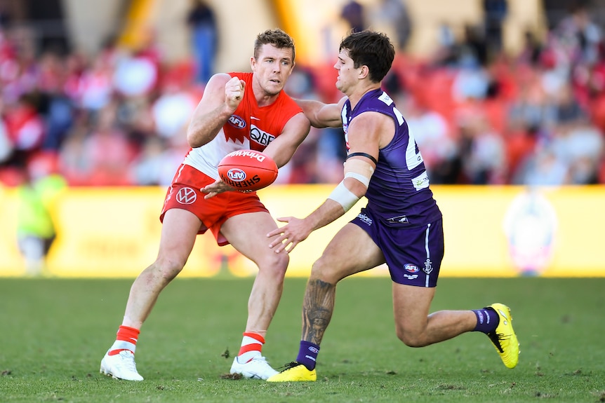 A Sydney Swans player handballs the ball away as a Fremantle player tries to lay a tackle. 