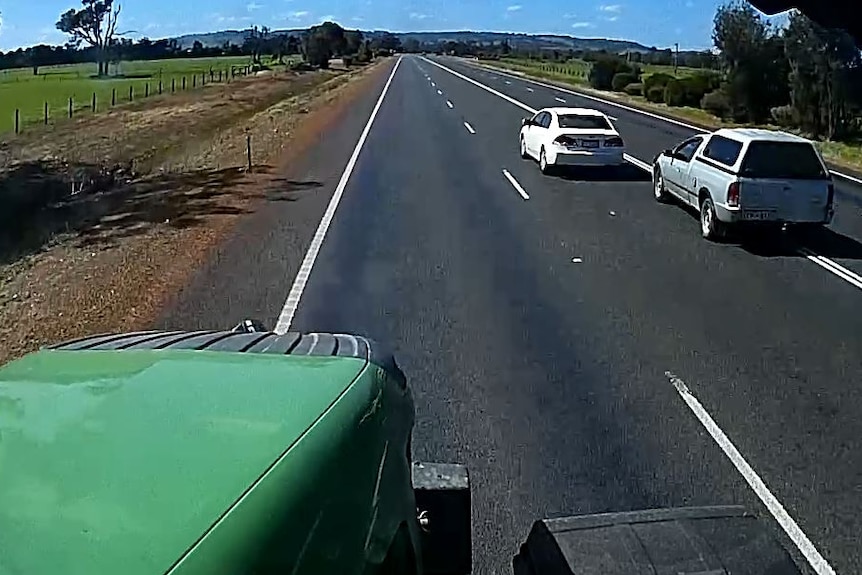 A video still showing two cars overtaking a tractor and crossing double white lines