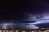 Dark clouds and lightning bolts at night time, above a regional city.