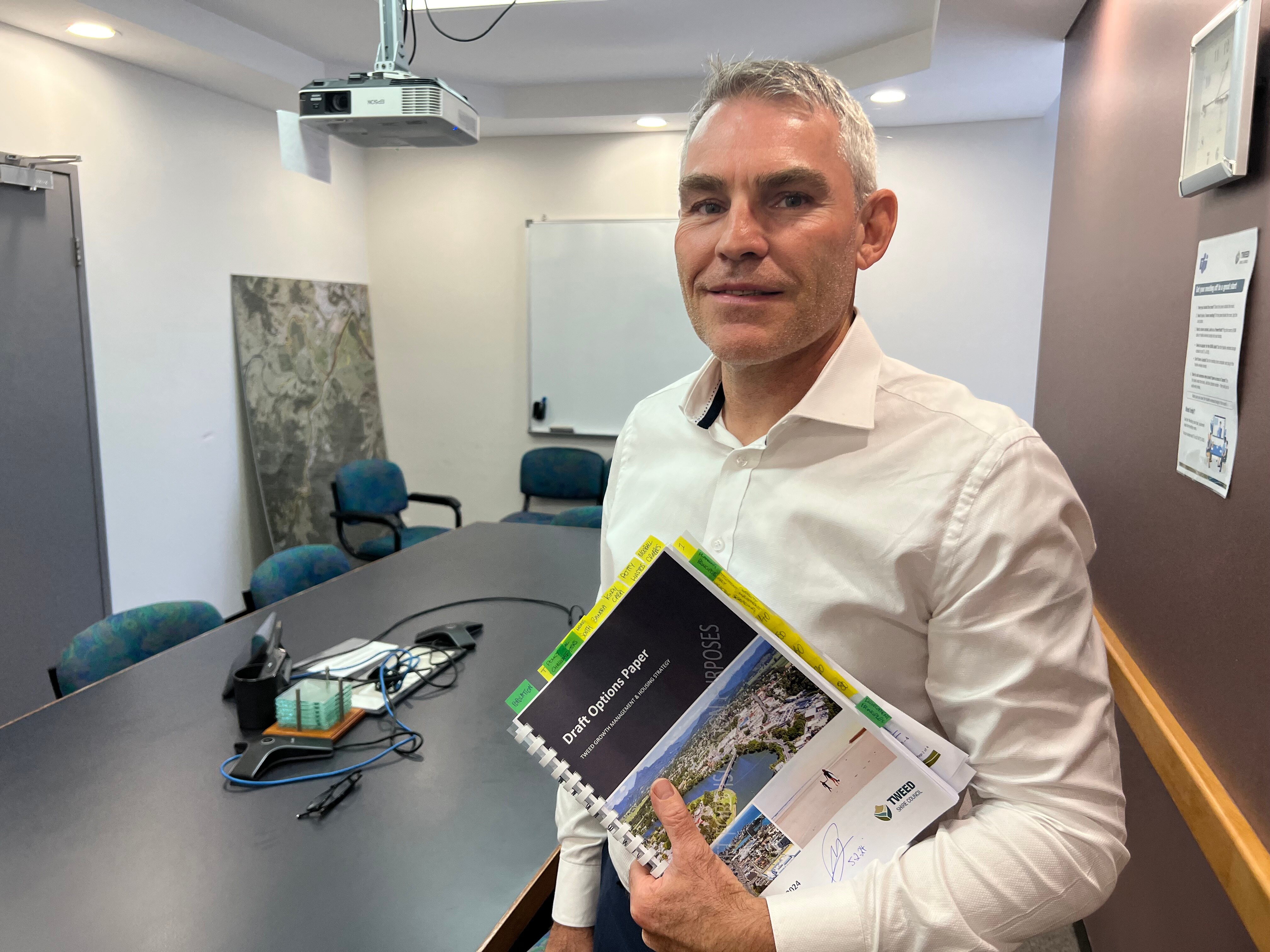 A man in an office holding up a document titled draft options paper.