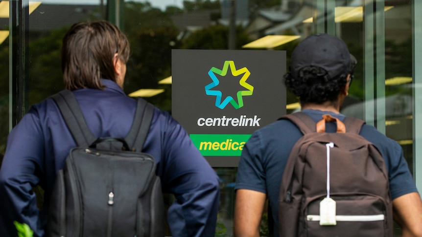 Two people standing with their backs to us looking at a Centrelink sign