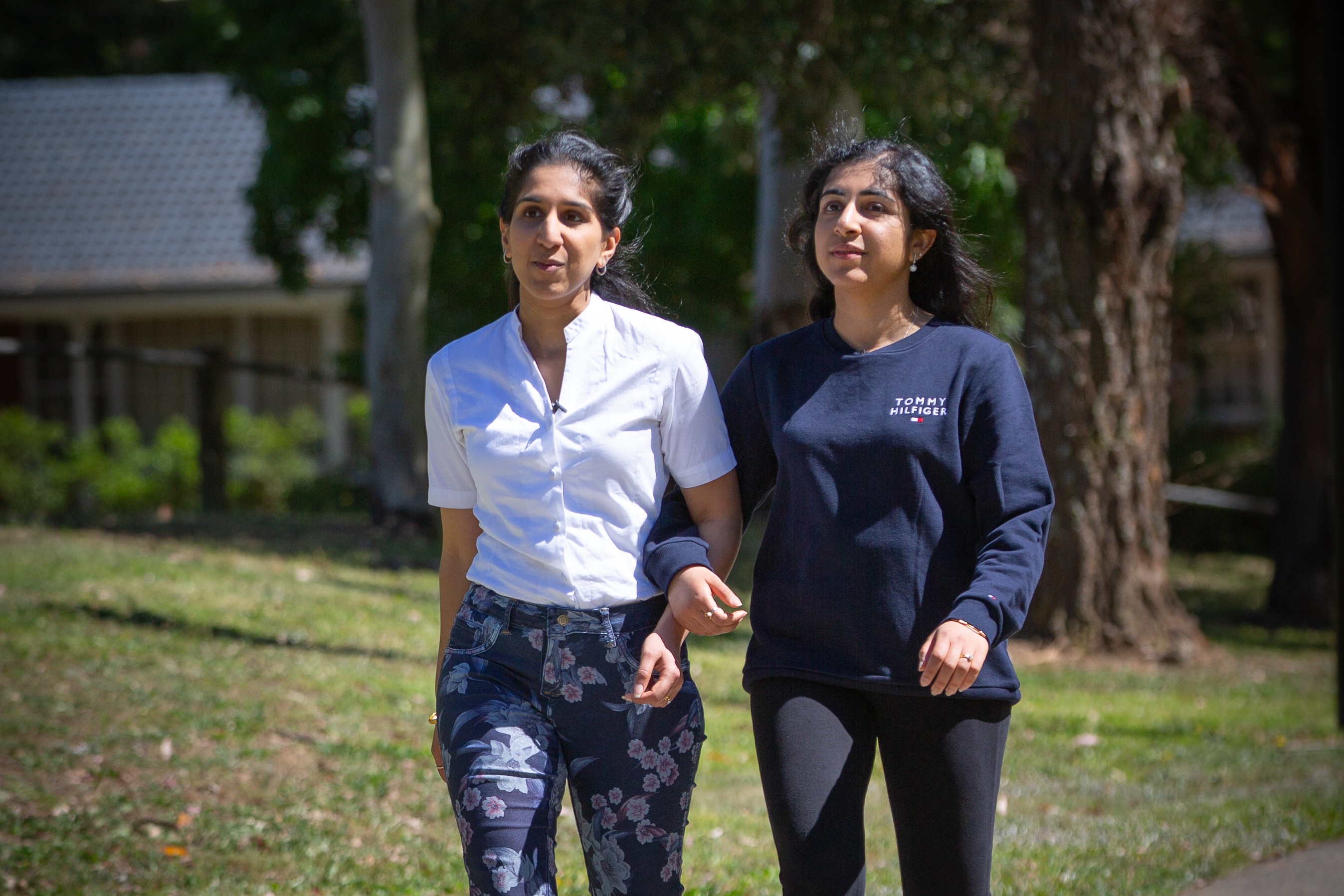 Dos mujeres caminan por un parque con los brazos cruzados.