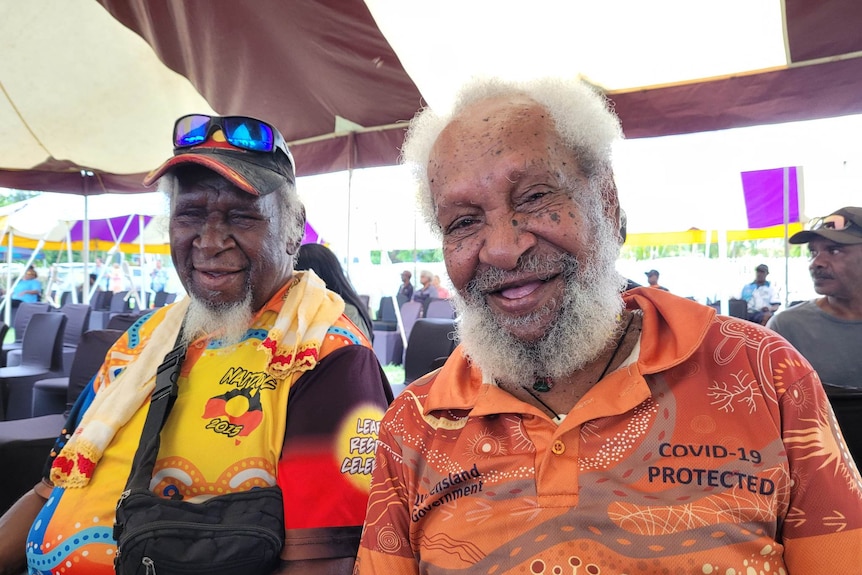 Two men sit next to each other smiling at the camera.