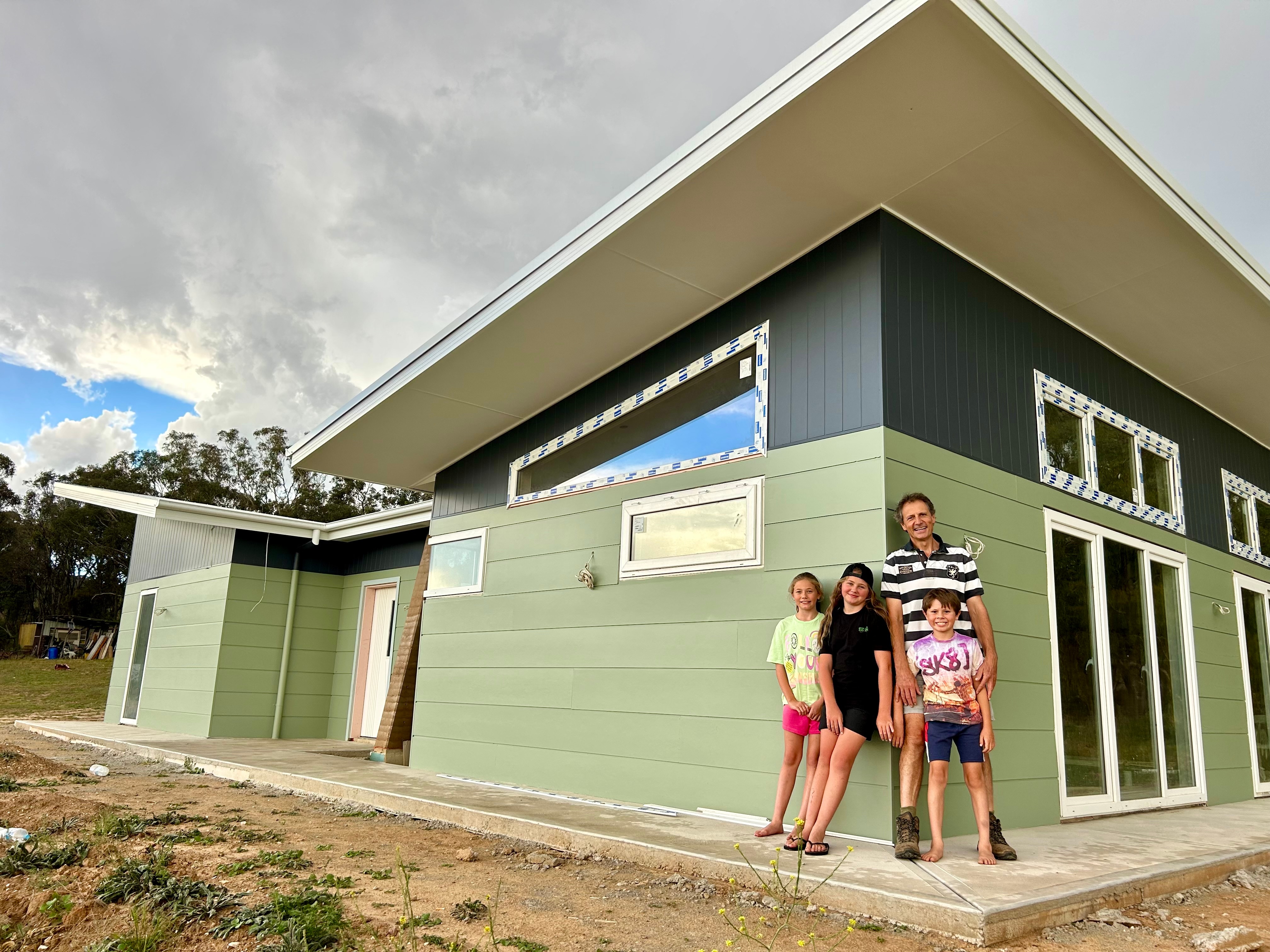 A father and his two daughters and son stand in front of a home on an overcast day.