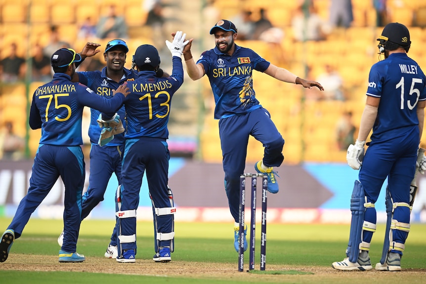 Sri Lankan players celebrate together as an English batter looks on bemused