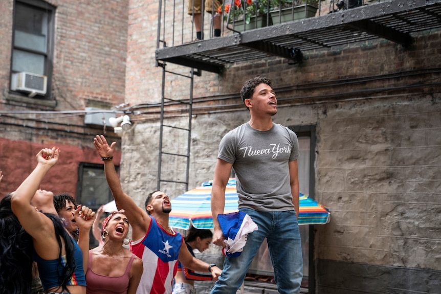 Anthony Ramos, a young Latino standing in the street with friends cheering him on, In The Heights 