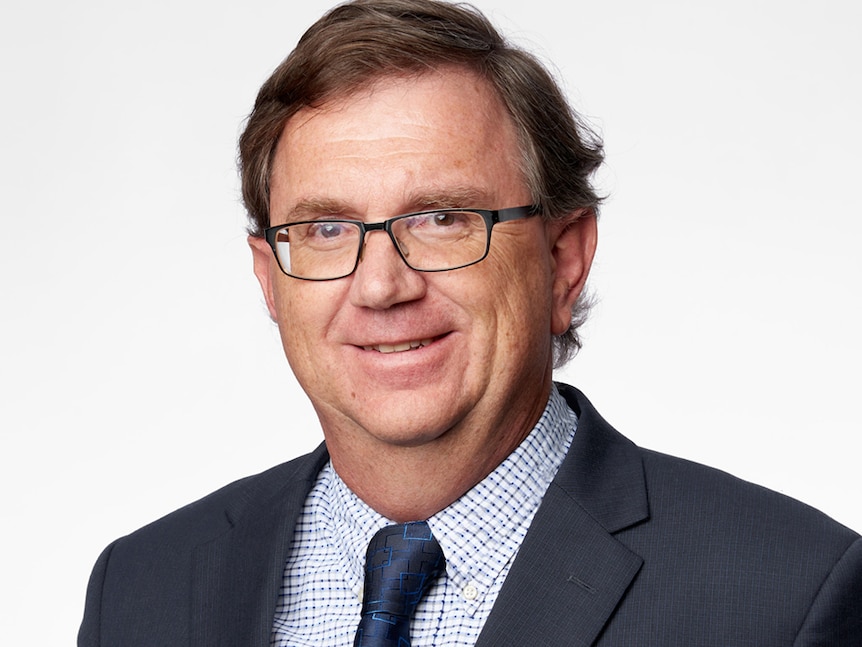 A corporate headshot of bespectacled man with dark hair, smiling and wearing a suit.