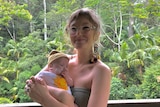 Alana Wilkinson smiling while holding baby Rafferty, trees behind them