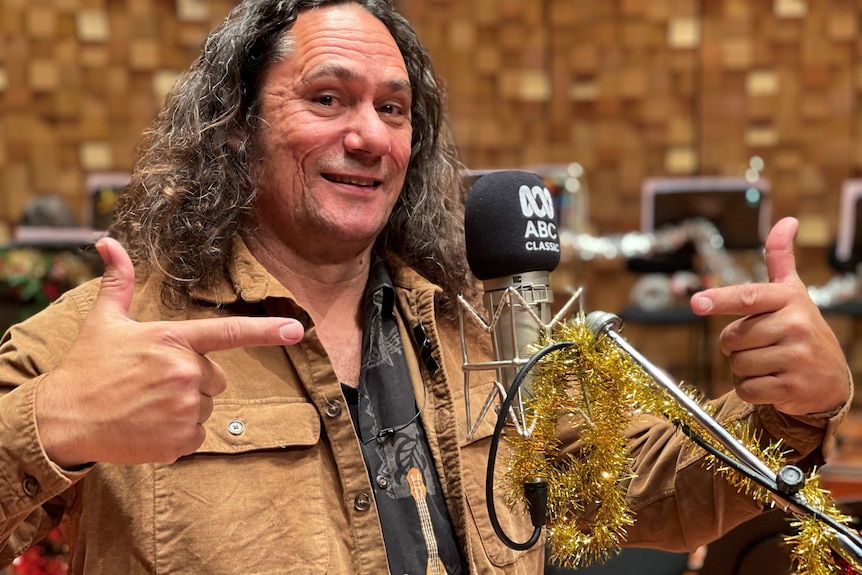 ABC presenter Clarence Slockee points with both hands at a microphone with and ABC Classic logo on the cover.