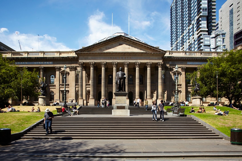 The facade of a grey, stone building, with several pillars at its front and stairs leading up to it