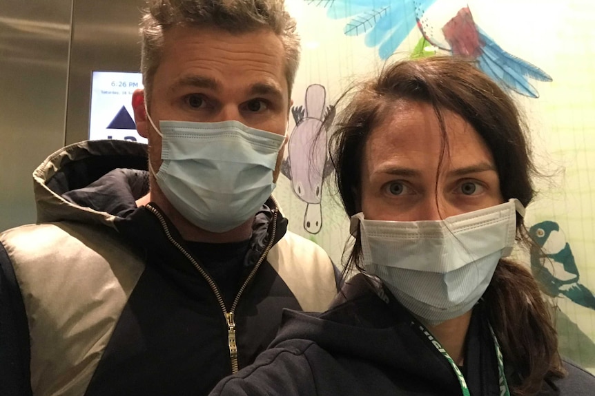 A man and a woman in face masks take a selfie in a hospital.