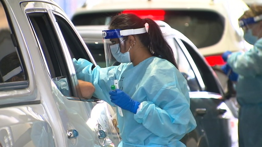 A picture of a woman in protective gear leaning into a car to do a COVID test.