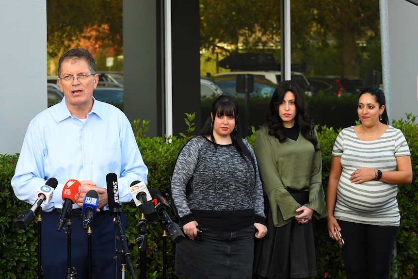 Ted Baillieu speaks to a podium of microphones outside as the three sisters watch on.