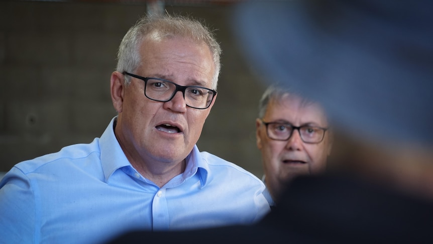 Scott Morrison speaking in Alice Springs looking toward the camera while wearing glasses and another person over his shoulder