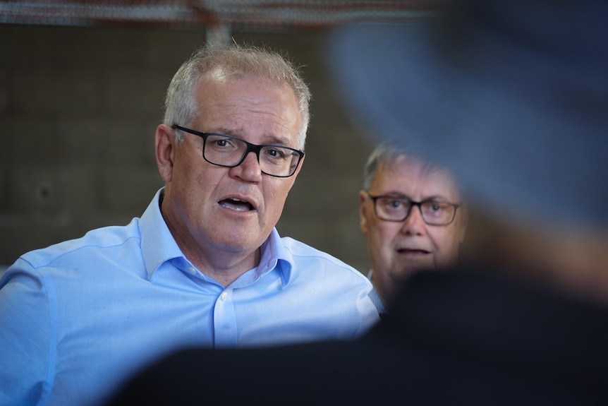 Scott Morrison parlant à Alice Springs regardant vers la caméra tout en portant des lunettes et une autre personne par-dessus son épaule