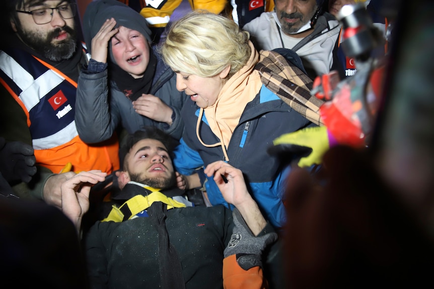 Teenager surrounded by rescuers and his mum after being pulled out from under rubble.