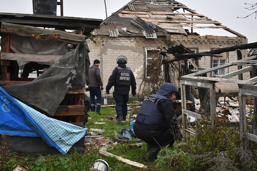 sappers in navy protective uniformas inspect a detroyed building which has had its roof blown off