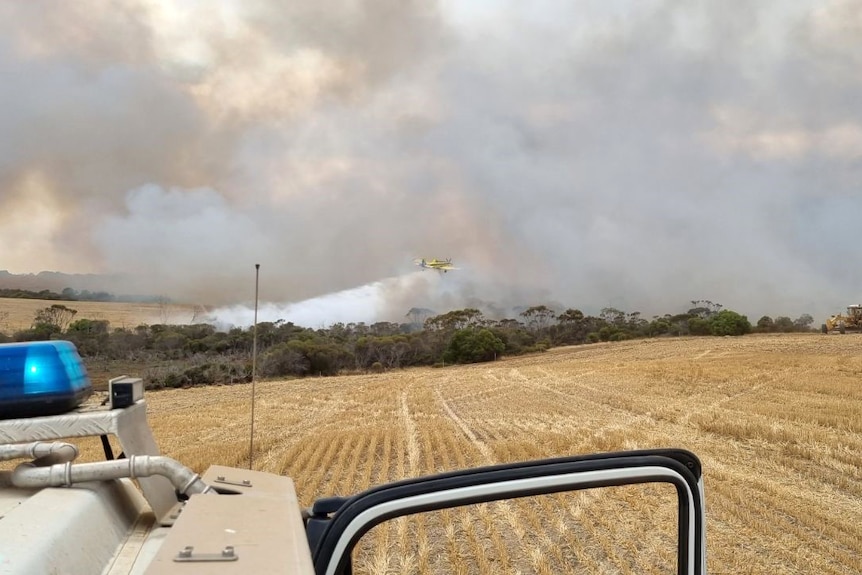 View over a dry paddock of smoke from a bushfire, with a firefighting vehicle in the left front corner