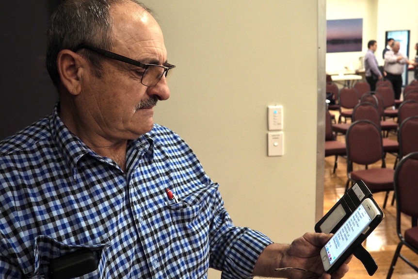 Grape grower Frank Dimasi looks at a text message on his phone with a serious expression on his face.