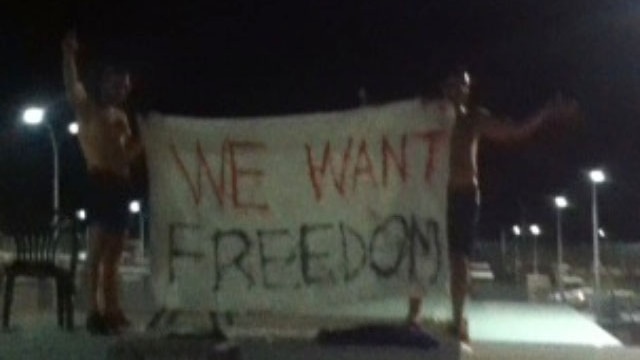 Two protesters hold a flag saying "we want freedom" at Yongah Hill detention centre.