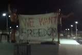 Two protesters hold a flag saying "we want freedom" at Yongah Hill detention centre.