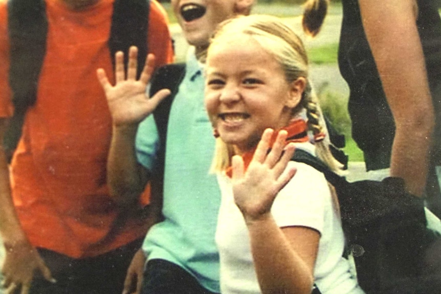 A little blonde girl waves to the camera