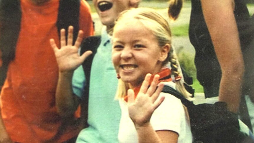 A little blonde girl waves to the camera