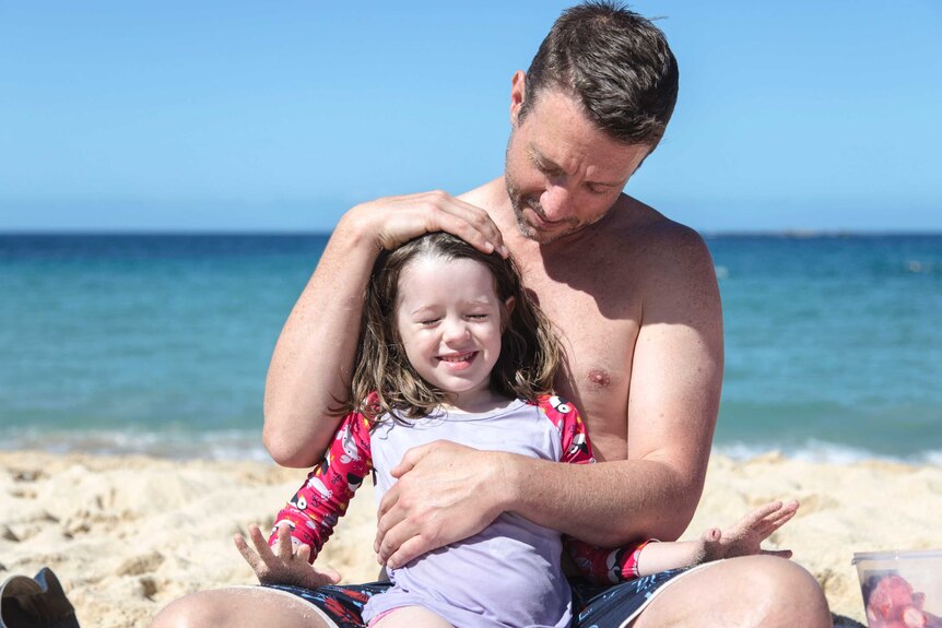 a man cuddling his young daughter in the sun on the beach