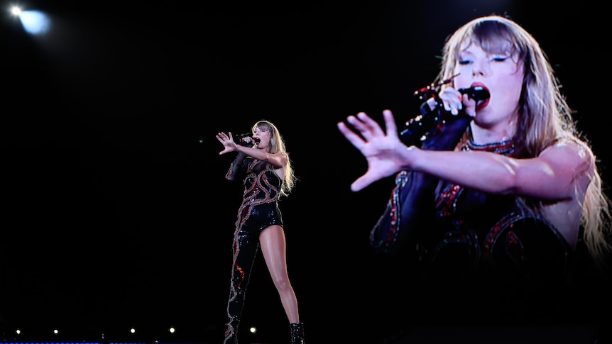 A female artist performs at night, on stage, singing into a microphone, reaching out to a crowd