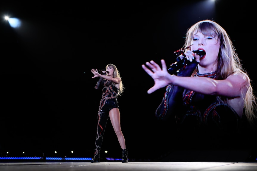 A female artist performs at night, on stage, singing into a microphone, reaching out to a crowd