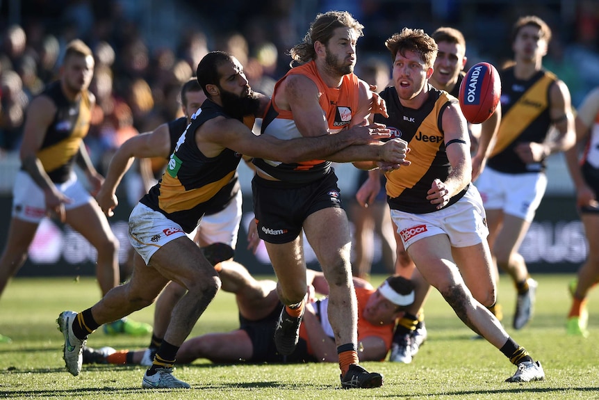 Callan Ward of the Giants attempts to hand pass the ball as he is tackled by Bachar Houli of the Tigers.