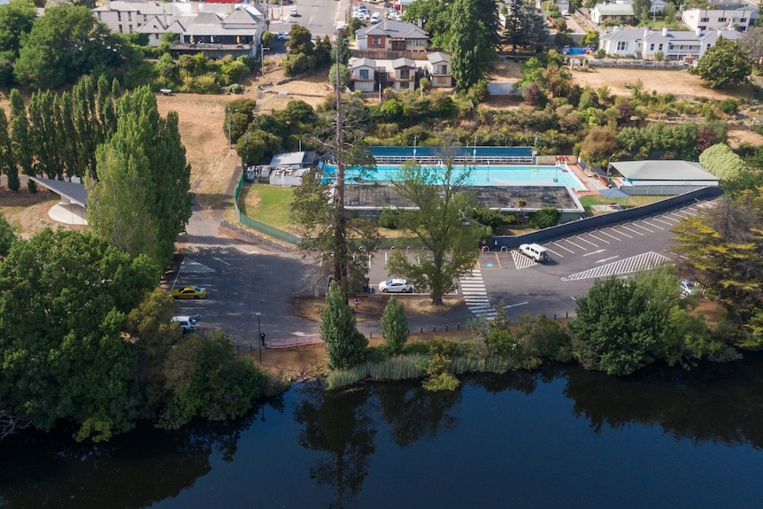 An aerial shot of a river next to a swimming pool and car park.