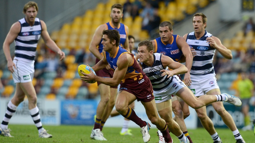 Brisbane Lions AFL player Simon Black runs with the ball trying to evade Geelong defenders.
