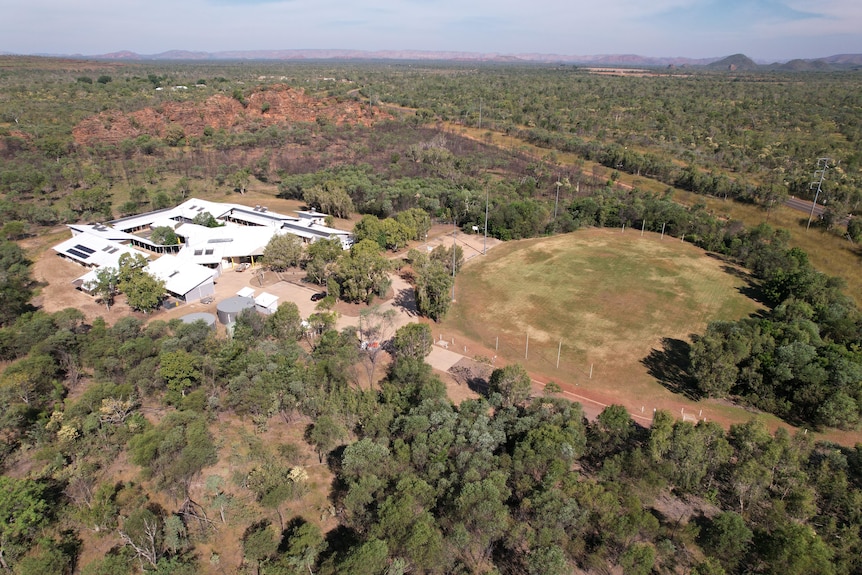 a drone image of a group of white building and a football oval surrounded by trees