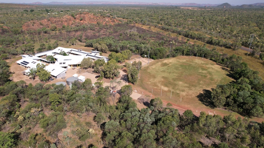 a drone image of a group of white building and a football oval surrounded by trees