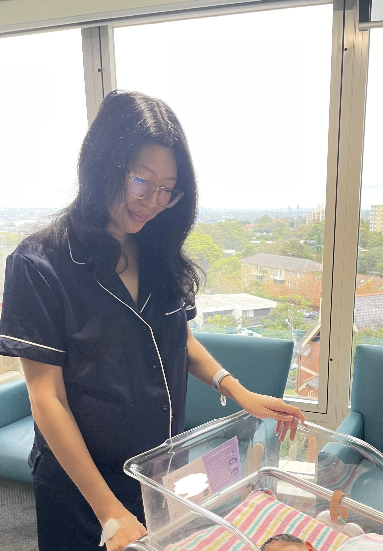 Tash Lay looks down at a hospital crib with her newborn baby in it.