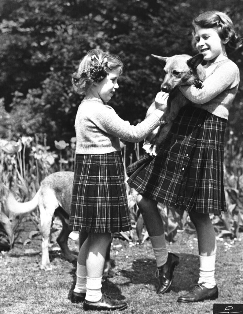 A young Princess Elizabeth, holds a Pembrokeshire Corgi as her sister Princess Margaret feeds it a biscuit.