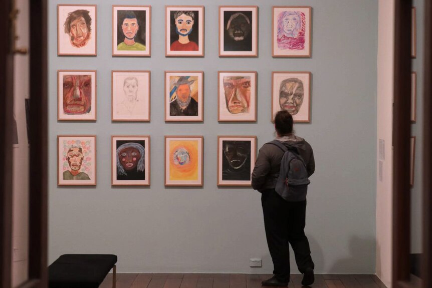 A lady is pictured from behind looking at artwork hanging on a wall