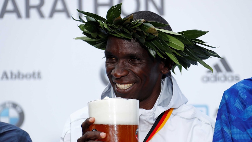 Eliud Kipchoge smiles as he poses with a stein of beer.