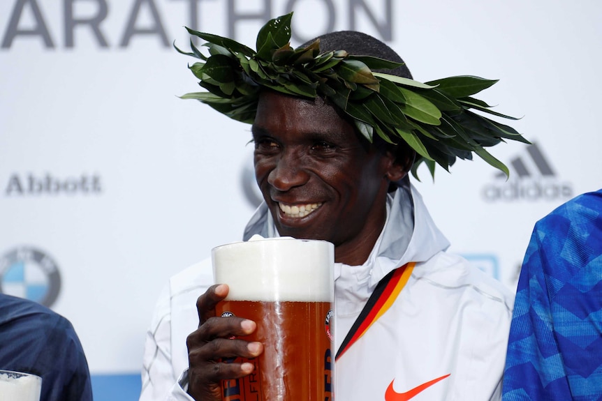 Eliud Kipchoge smiles as he poses with a stein of beer.